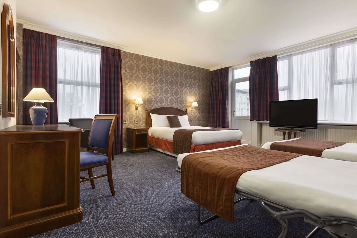A hotel room with two beds, a desk, a chair, a TV, and two wall-mounted lamps.
