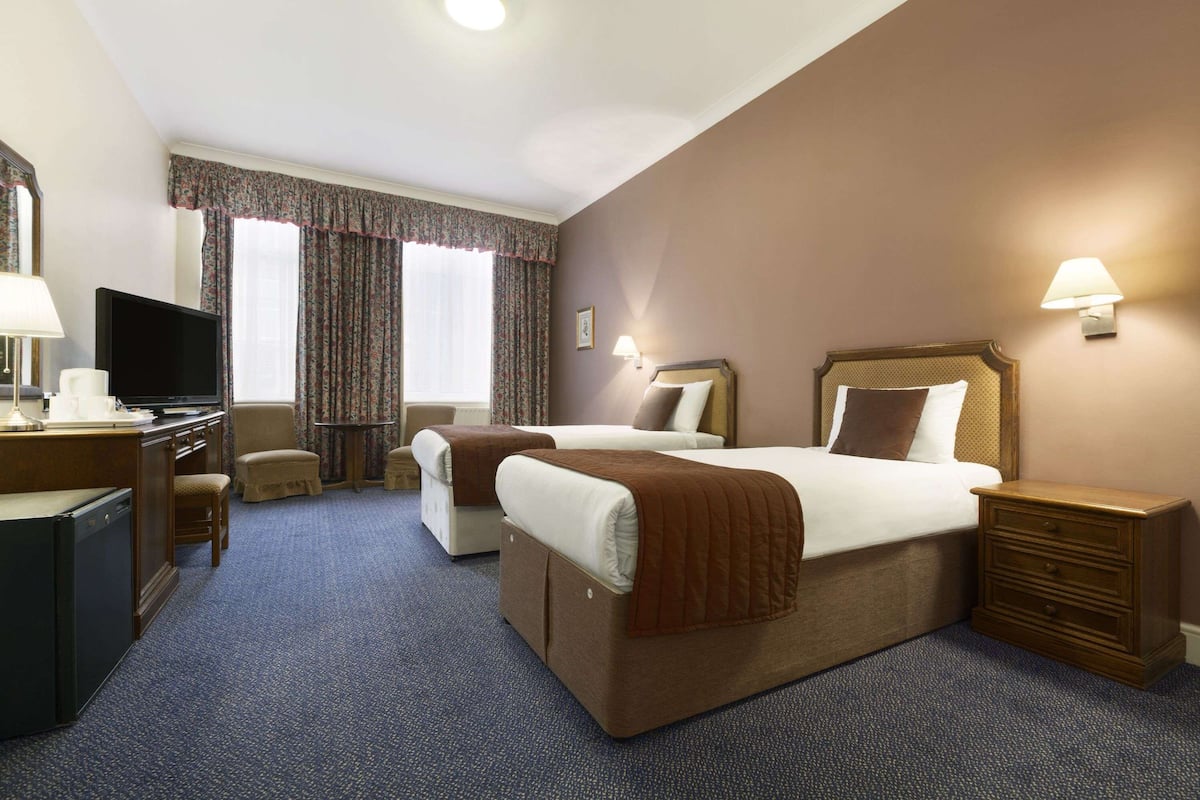 A hotel room with a large bed, a desk with a television, a chair, and a dresser.