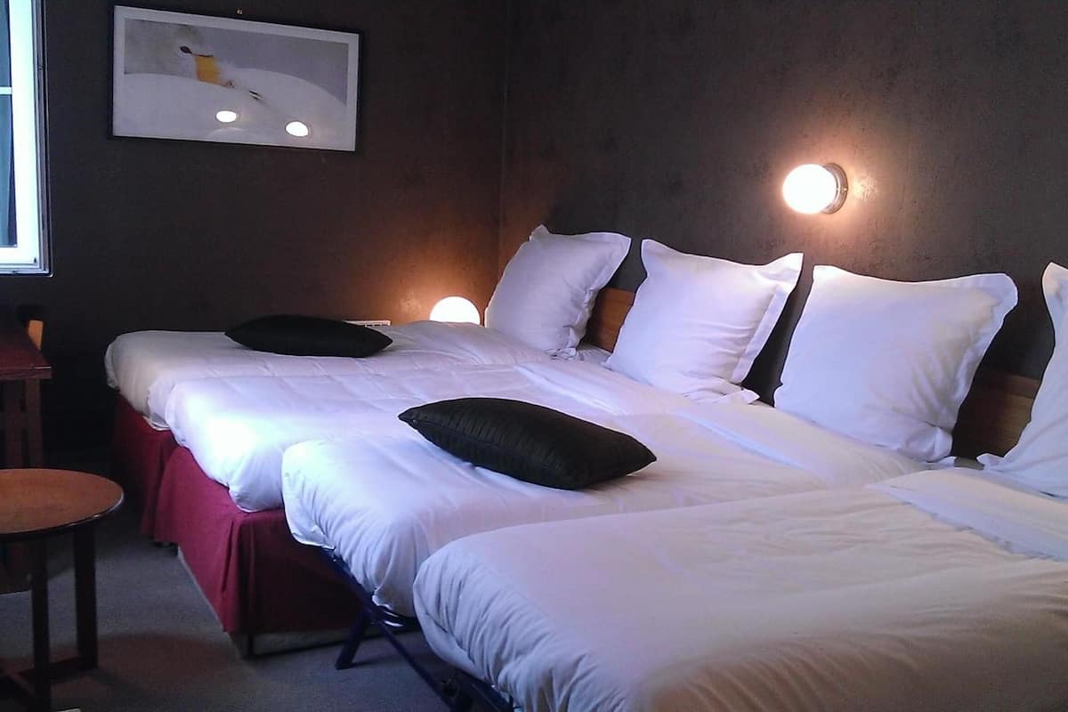 Une chambre d’hôtel avec un grand lit, deux tables de chevet, une chaise et un luminaire fixé au mur.