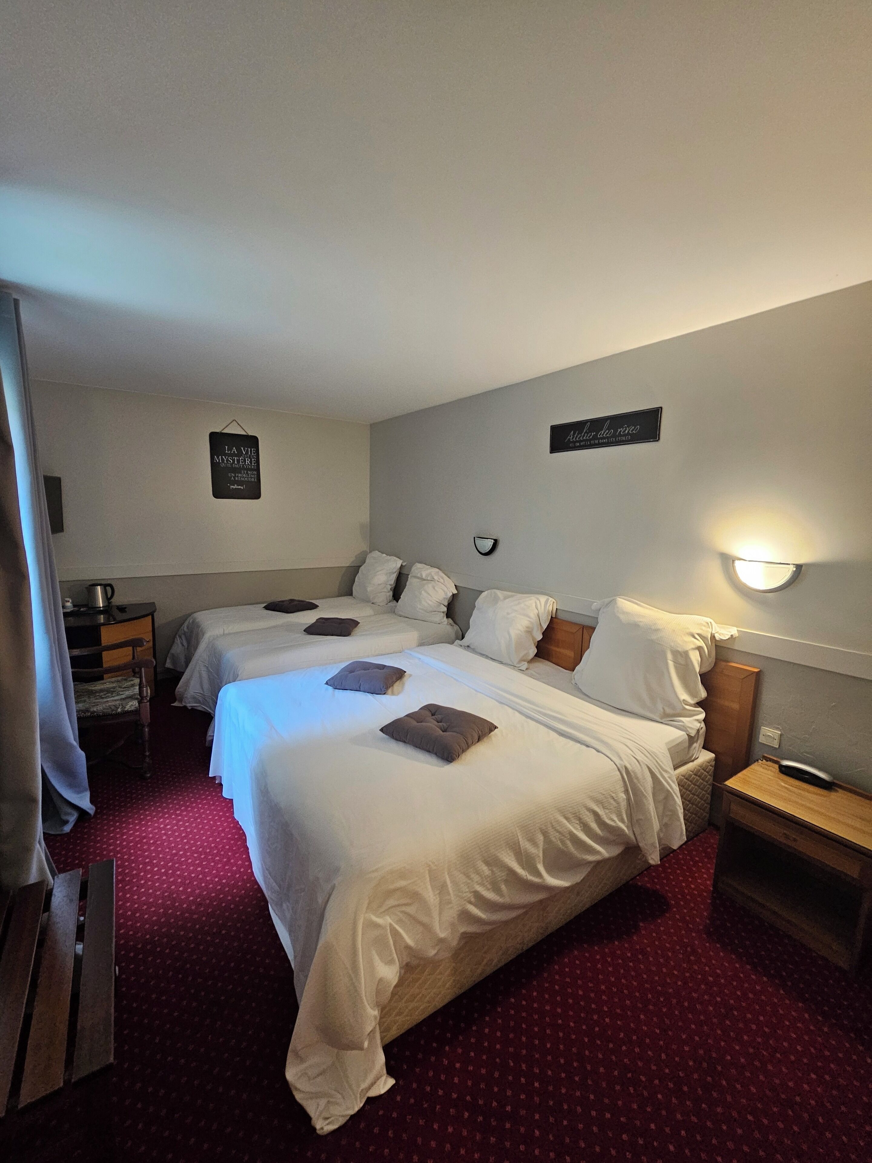 A hotel room with two beds, a wooden nightstand, a wall-mounted lamp, and a small table with a kettle.