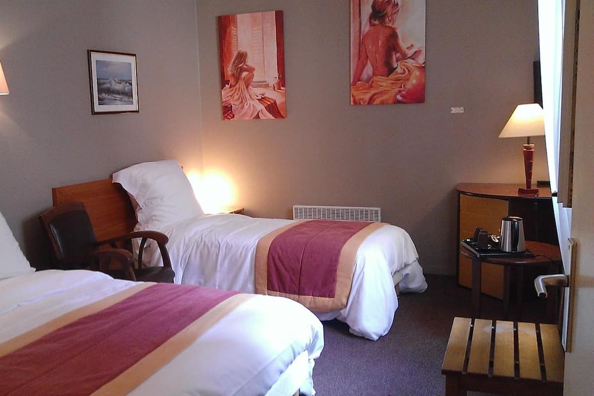 Une chambre d’hôtel avec deux lits, une table de chevet, une lampe et des œuvres d’art accrochées au mur.