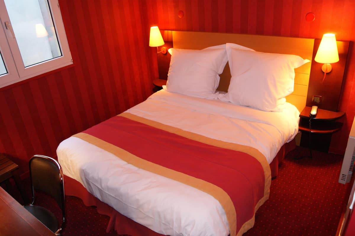 Une chambre d’hôtel avec un lit, deux lampes de chevet, une chaise et une fenêtre.
