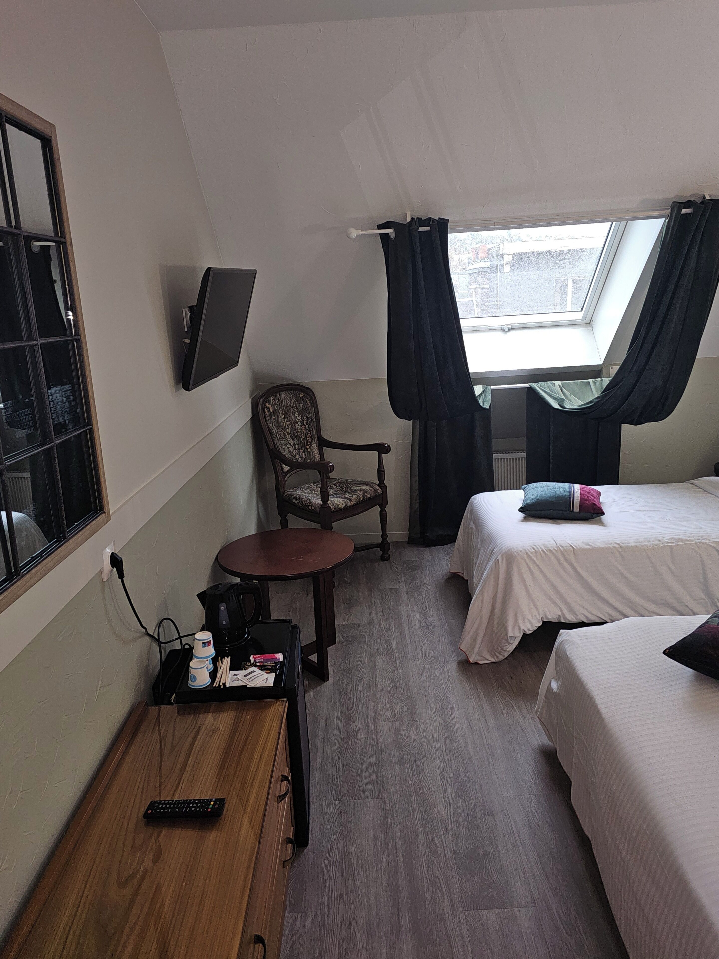 Une chambre d’hôtel avec deux lits, un bureau avec une télécommande, une chaise, un téléviseur fixé au mur et une fenêtre avec des rideaux.