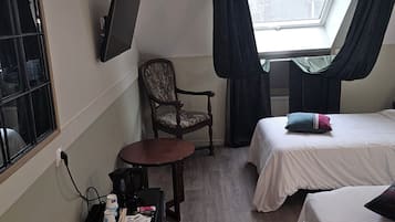 Une chambre d’hôtel avec deux lits, un bureau avec une télécommande, une chaise, un téléviseur fixé au mur et une fenêtre avec des rideaux.