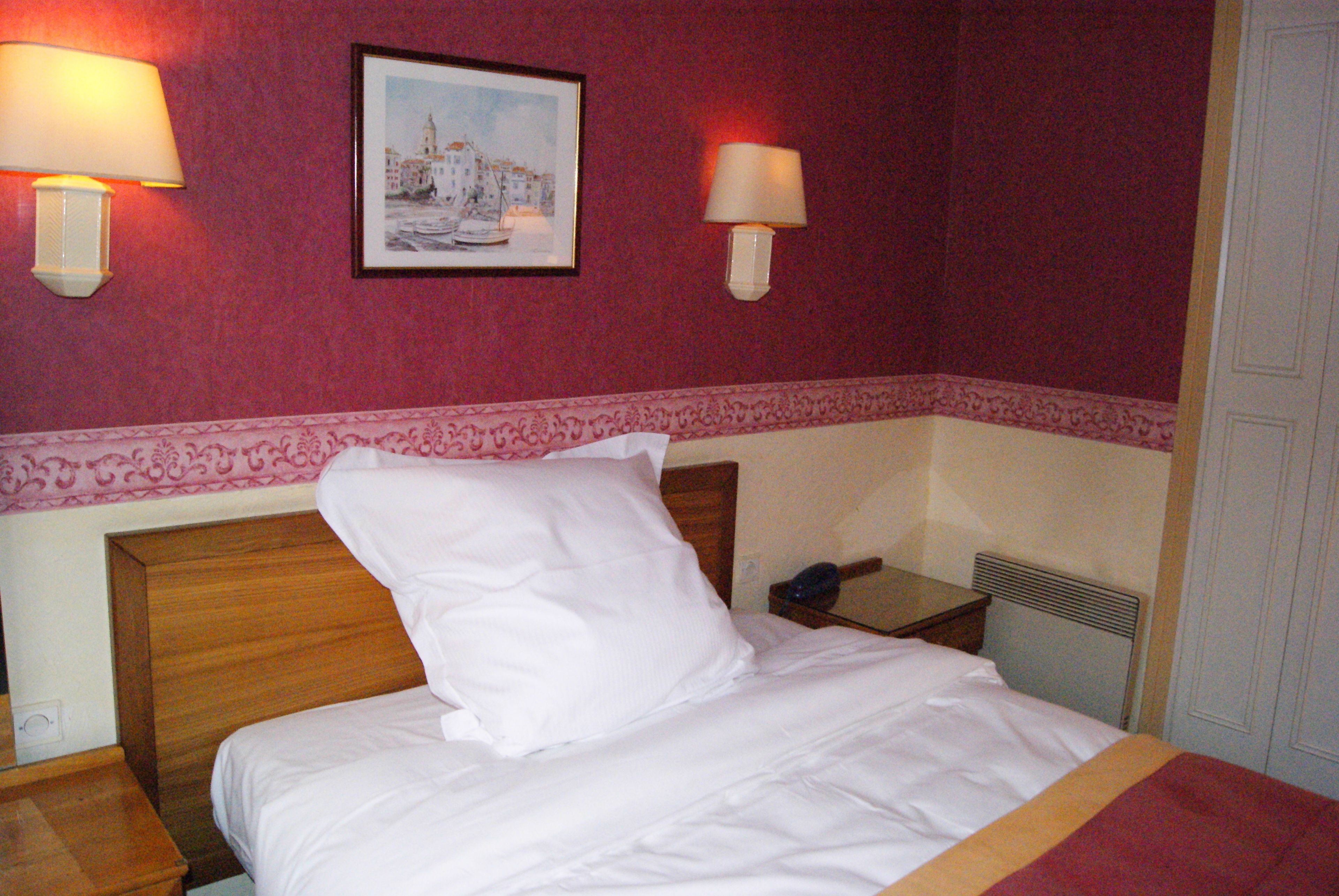 Une chambre d’hôtel avec un lit, deux lampes de chevet, un tableau encadré au mur et une table de chevet avec un téléphone.