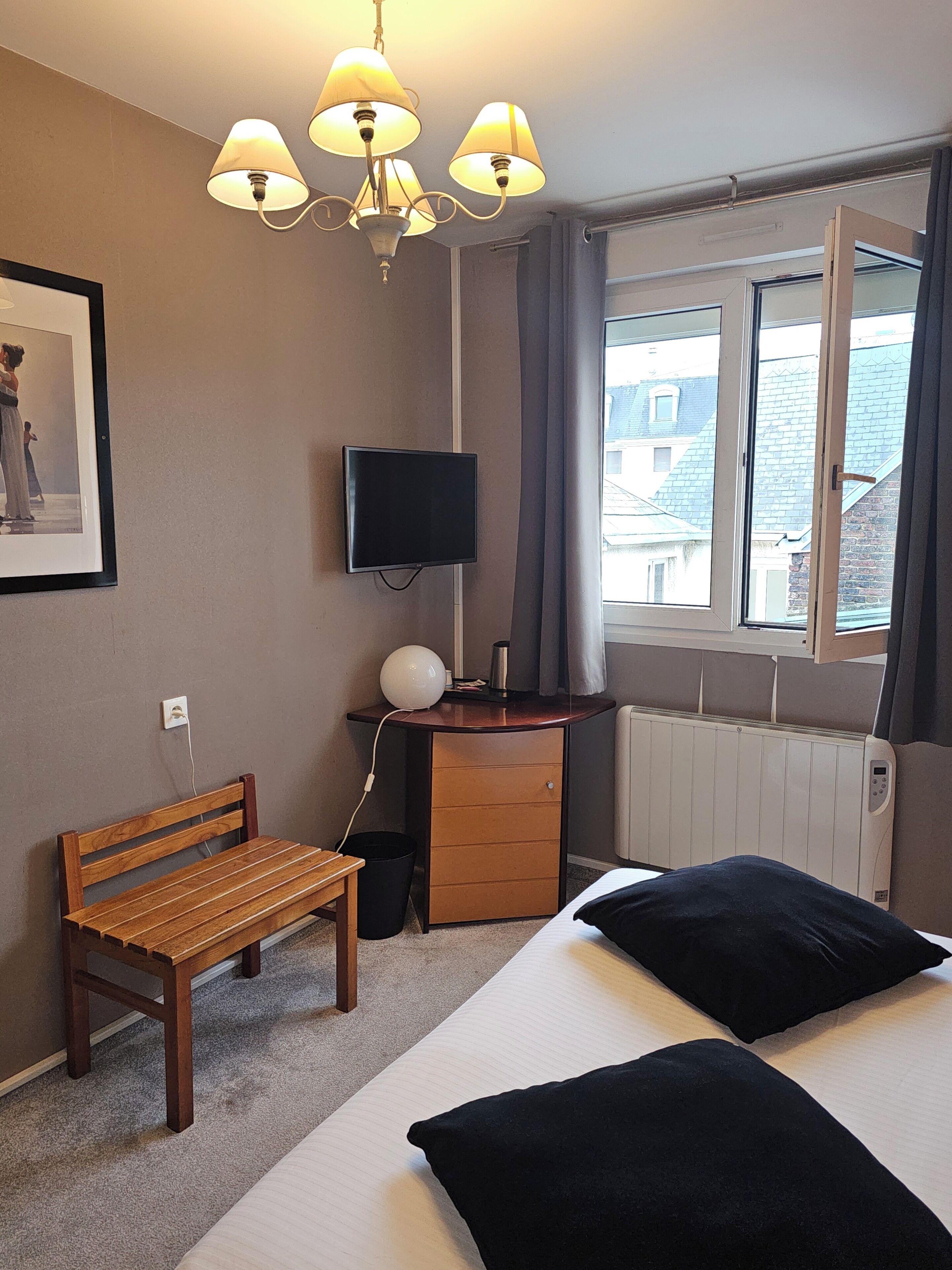 A bedroom with a bed, a desk with a TV, a chair, a window with curtains, and a radiator.