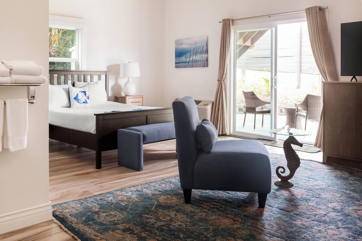 A bedroom with a bed, a chair, a desk, a lamp, a TV, and a view of the outdoors.