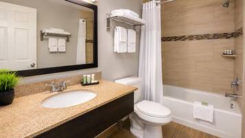 A modern bathroom with a granite countertop sink, a white toilet, a bathtub, and a shower with a curtain.