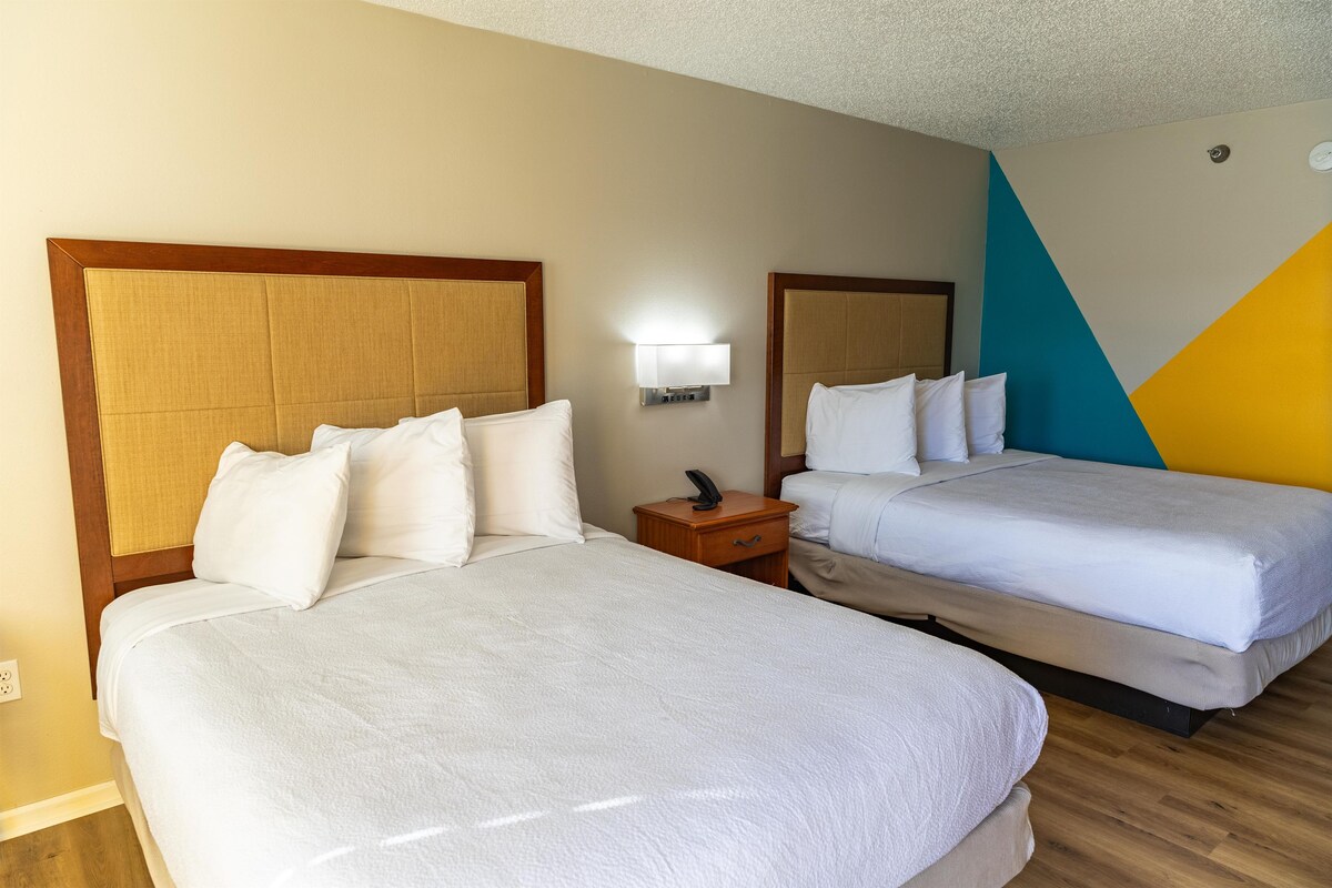 A hotel room with two beds, a nightstand, a wall-mounted lamp, and a geometric wall design.