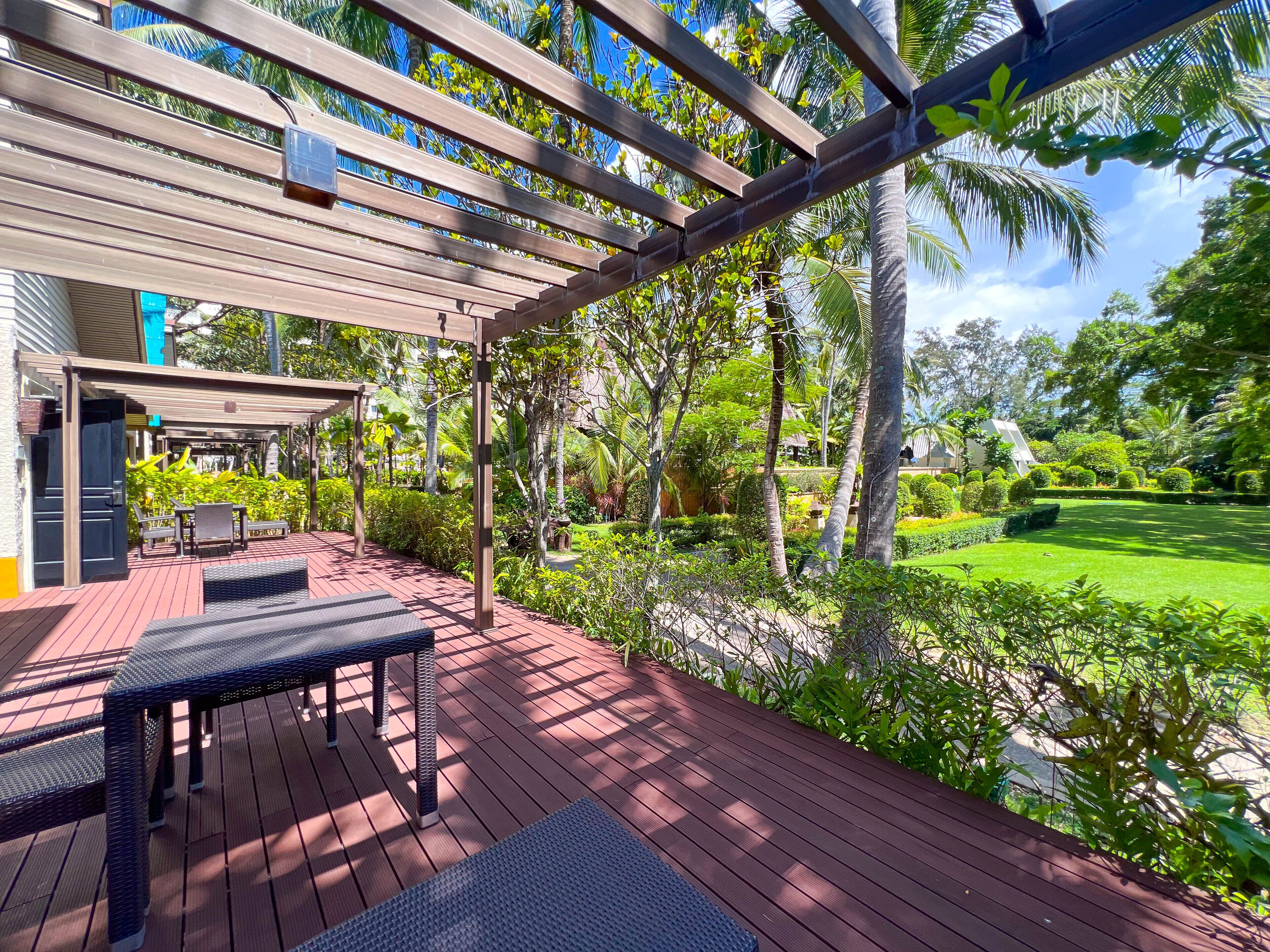 A covered outdoor area with a wooden deck, seating, and lush greenery.