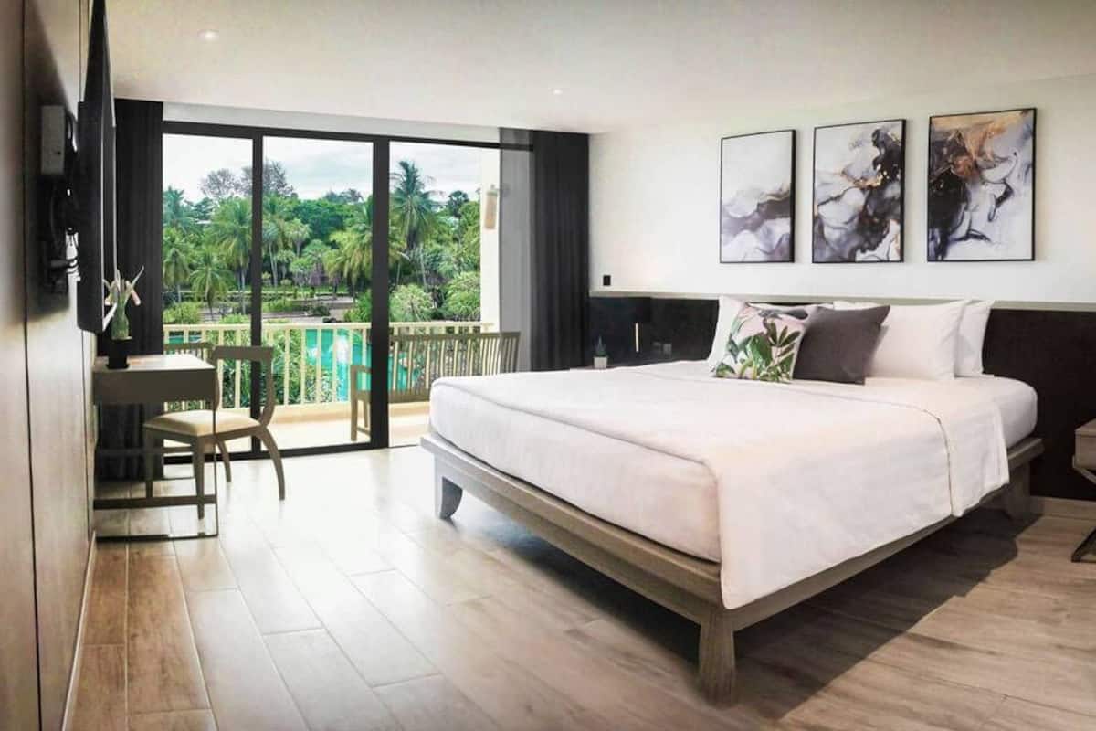 Une chambre moderne avec un grand lit, un bureau et un balcon offrant une vue sur la verdure.