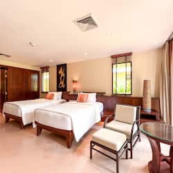 Two single beds with crisp linens and matching pillows, a nightstand, and a comfortable armchair.