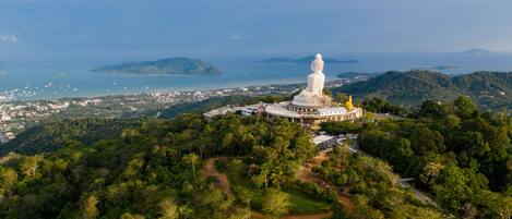 A large white statue on a hilltop with a view of a coastal town and the sea.