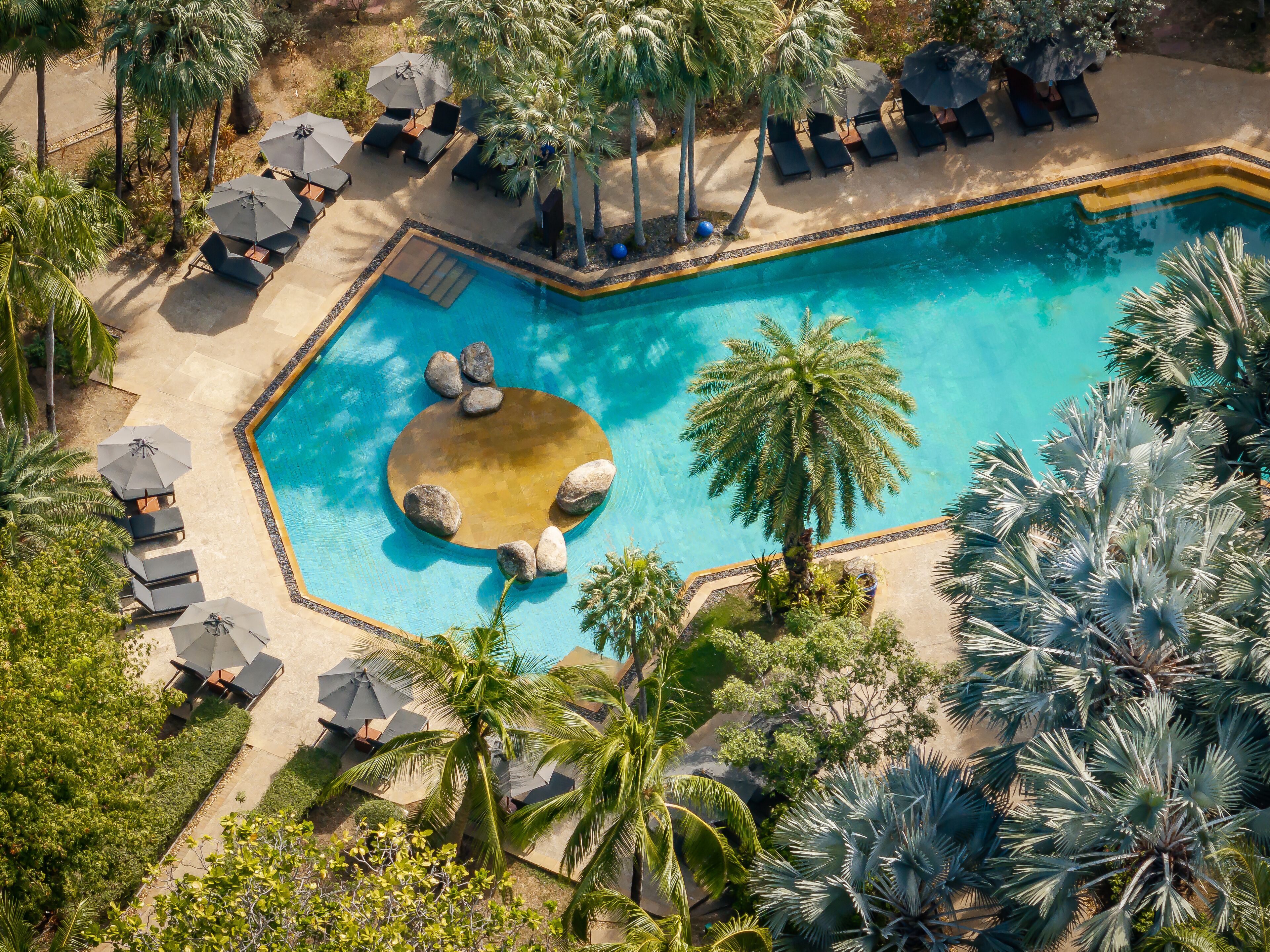 An aerial view of a pool area with lounge chairs, umbrellas, and palm trees.