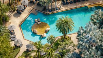 An aerial view of a pool area with lounge chairs, umbrellas, and palm trees.
