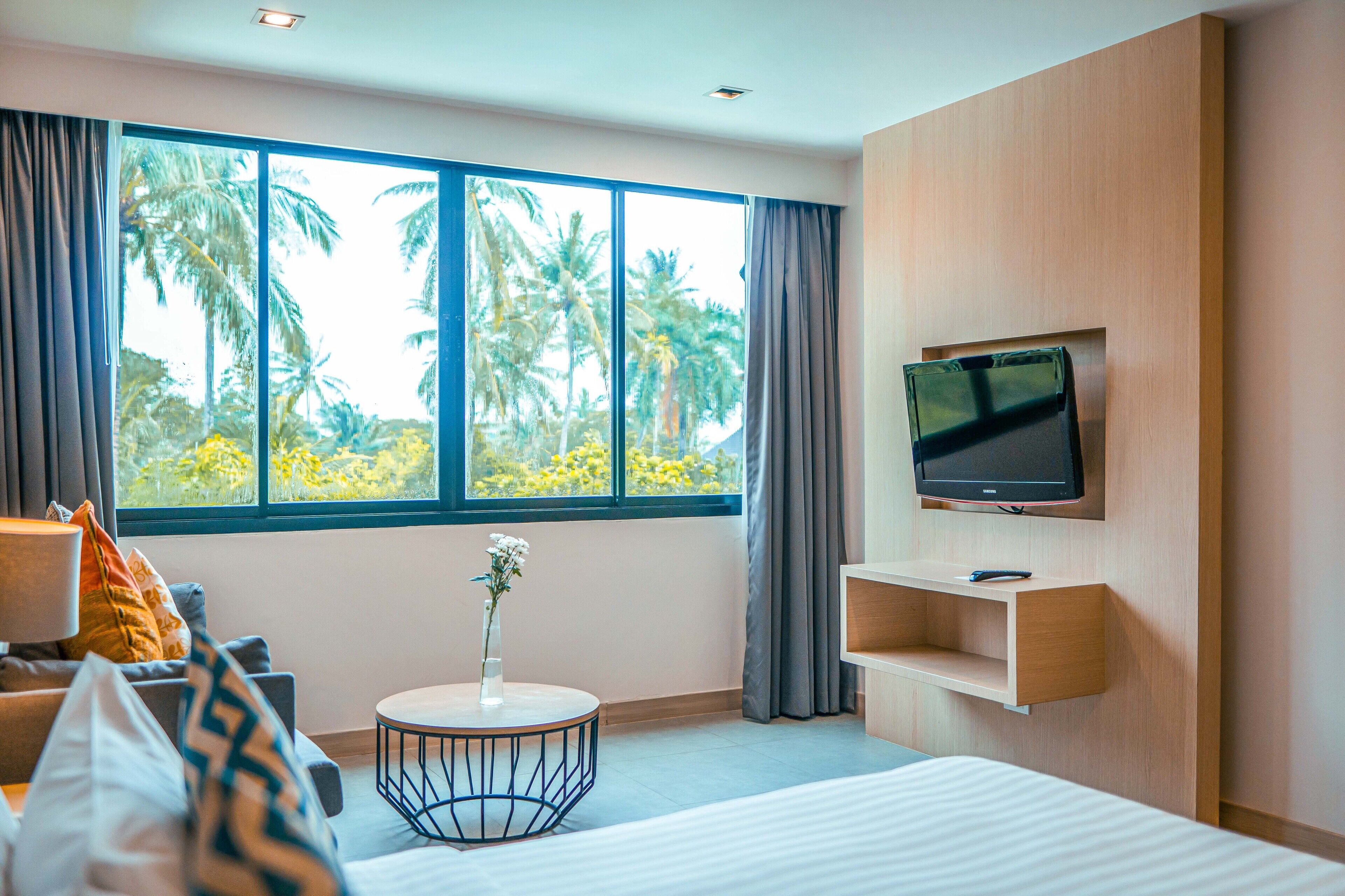 Una habitación de hotel moderna con un ventanal grande, una cama, una mesita de centro redonda, un televisor montado en la pared y un estante pequeño.