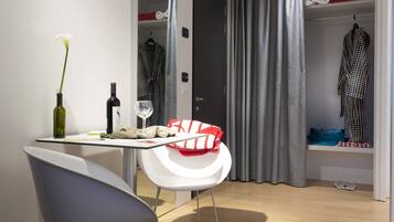 A modern hotel room with a dining area, a mirror, a robe, and a closet.