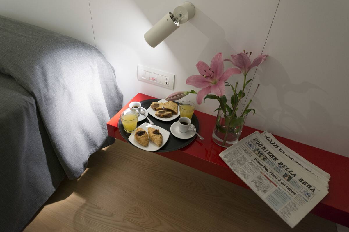 A neatly arranged breakfast table with croissants, a cup of coffee, and a glass of orange juice. A newspaper titled "Gazzetta della Sera" is also visible.