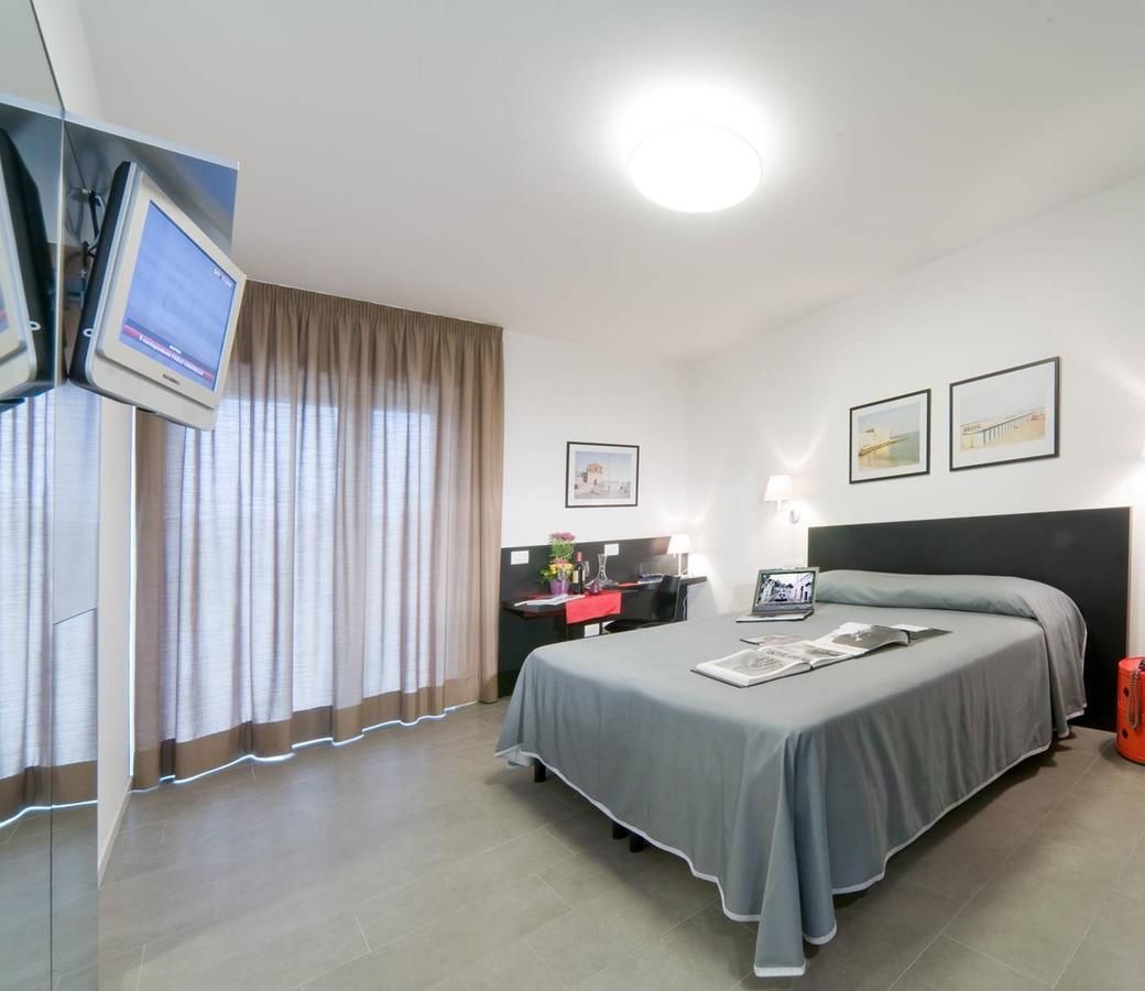Ein Hotelzimmer mit einem Bett, einem Schreibtisch mit Computer, einem an der Wand montierten Fernseher und zwei gerahmten Bildern.