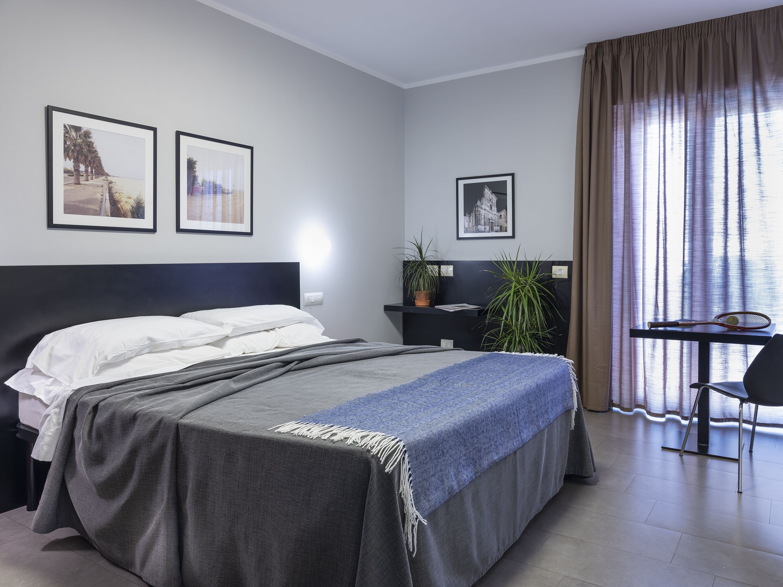 A modern hotel room with a bed, a desk, and two framed pictures on the wall.