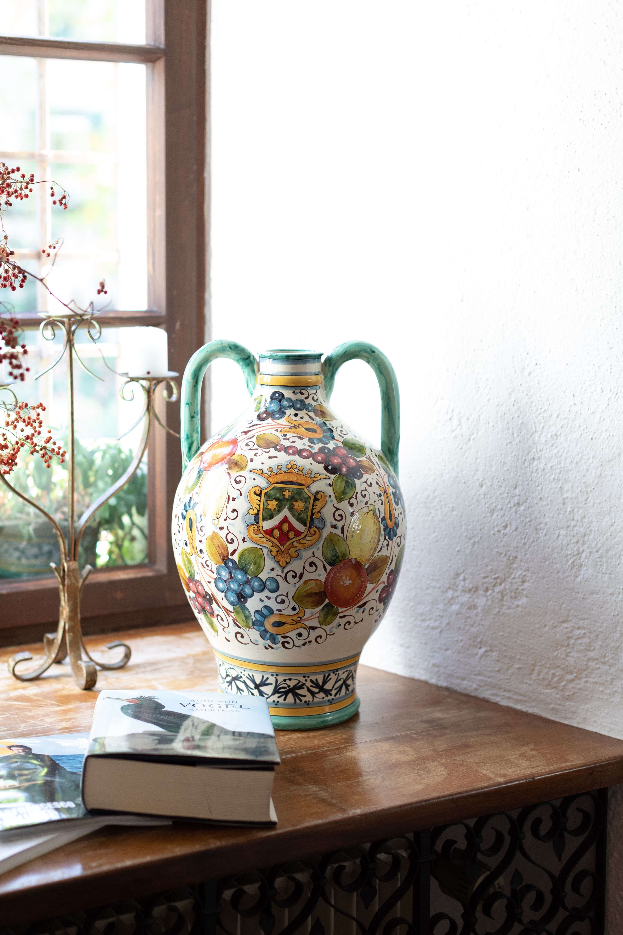A ceramic jug with floral patterns on a wooden table near a window.