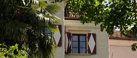 A building with a tiled roof, a balcony, and a window with shutters.