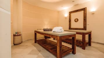 A wooden bench with a cushioned seat and a small table beside it, both placed on a tiled floor in a room with a large mirror and a decorative wall piece.