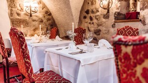 Un comedor con paredes de piedra, manteles blancos y sillas rojas con estampado.