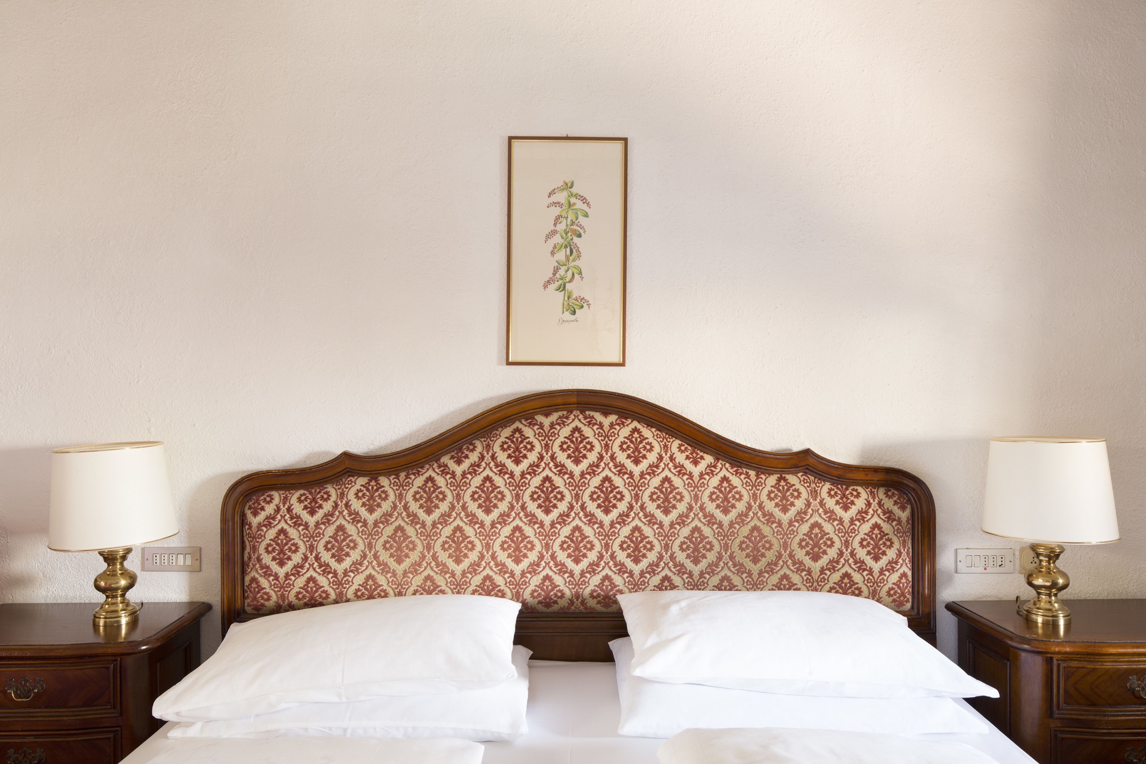 A neatly made bed with white linens, a patterned headboard, and two bedside tables with lamps.