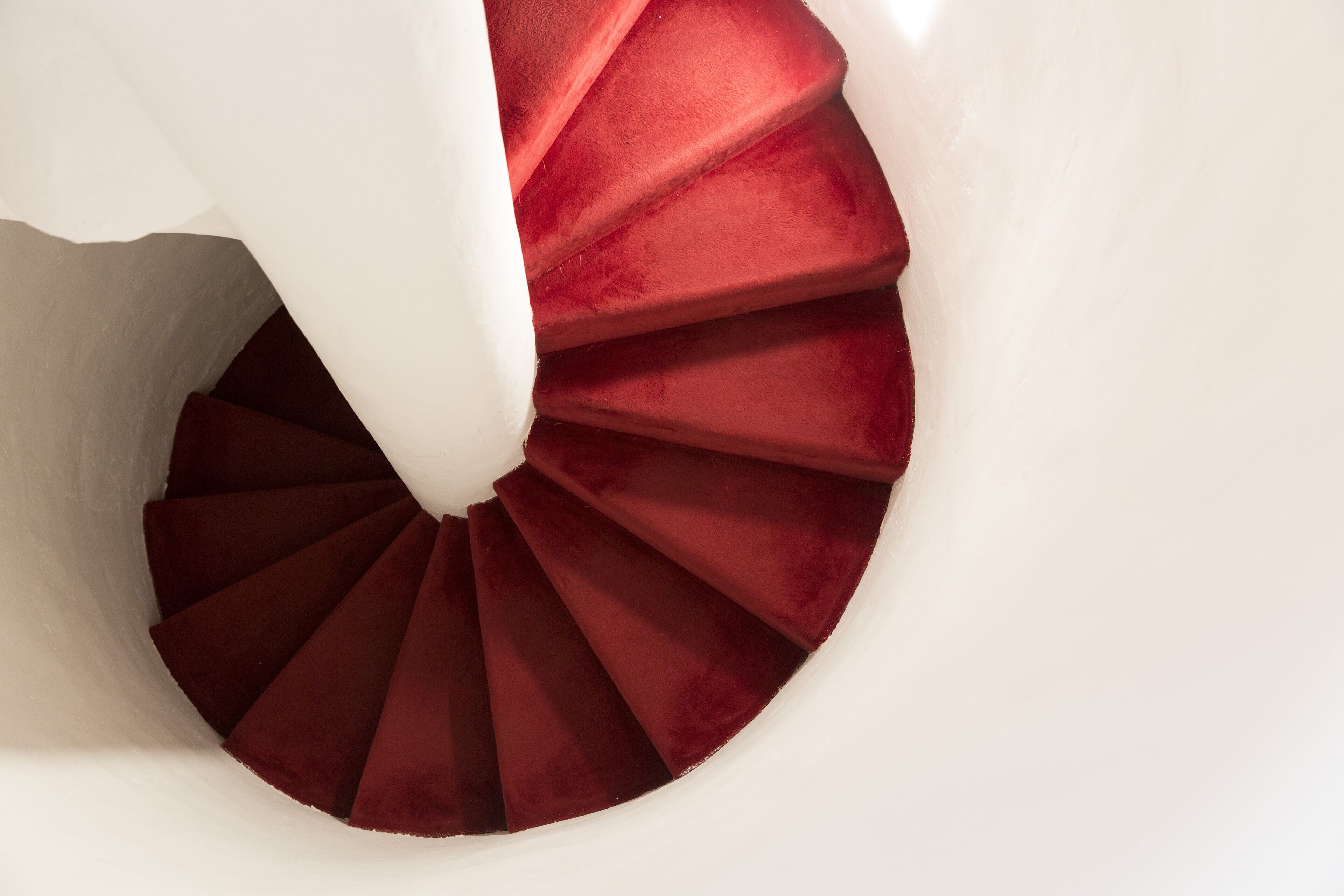 A spiral staircase with a white wall and red steps.