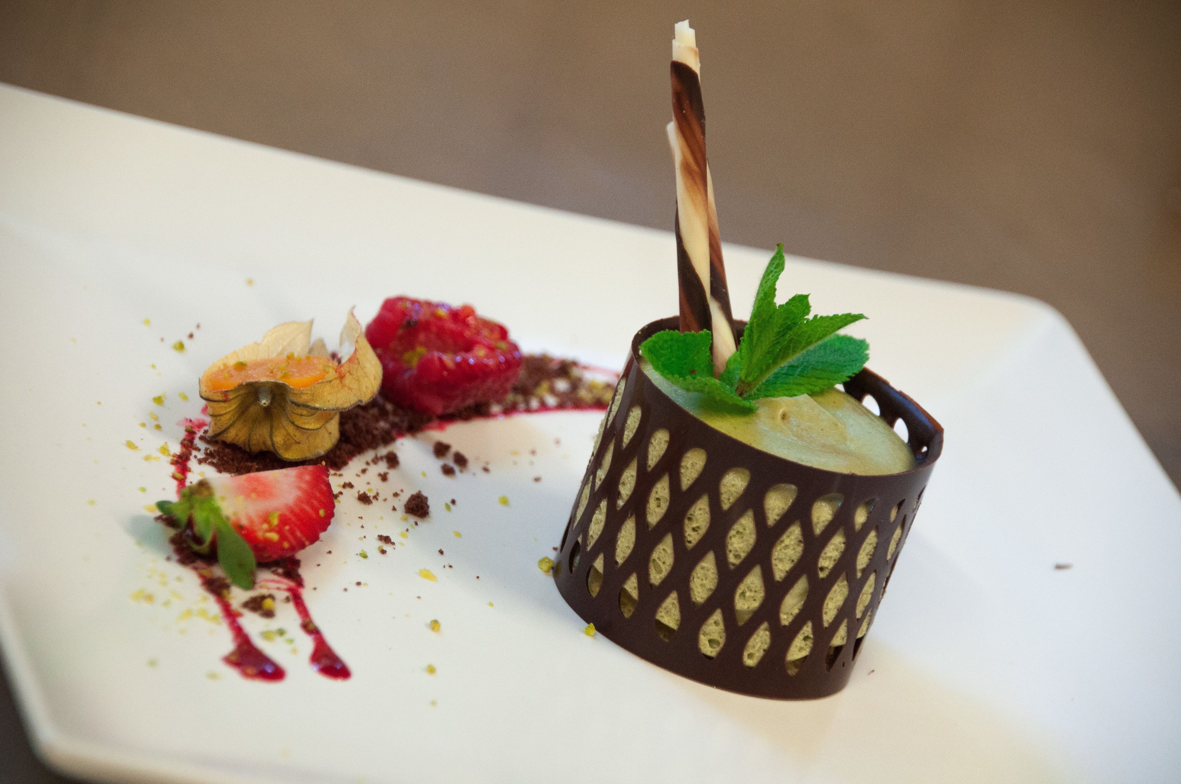 A dessert on a white plate with a chocolate cup and a strawberry.