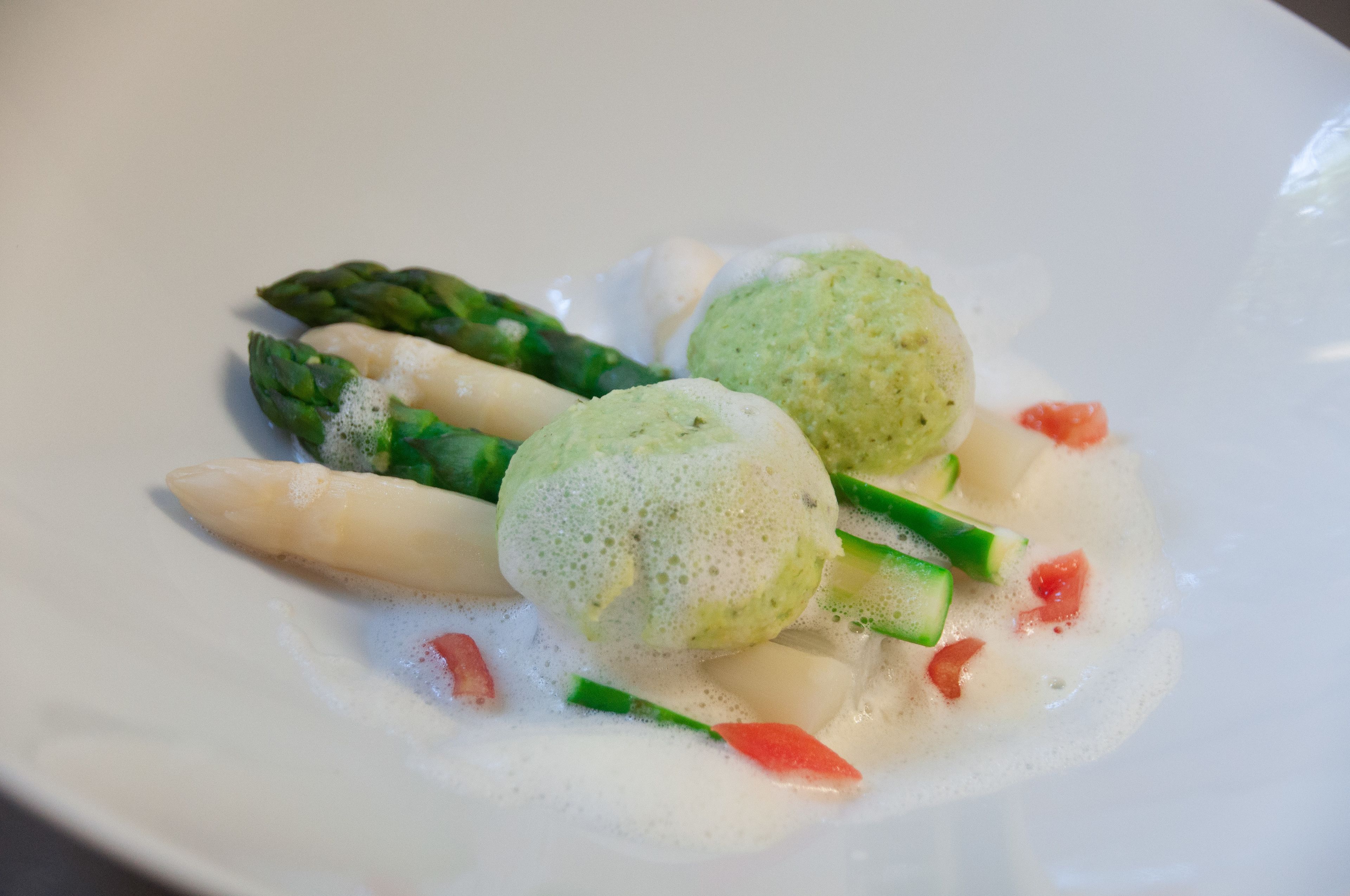 A plate with two green dumplings, asparagus, and diced tomatoes.