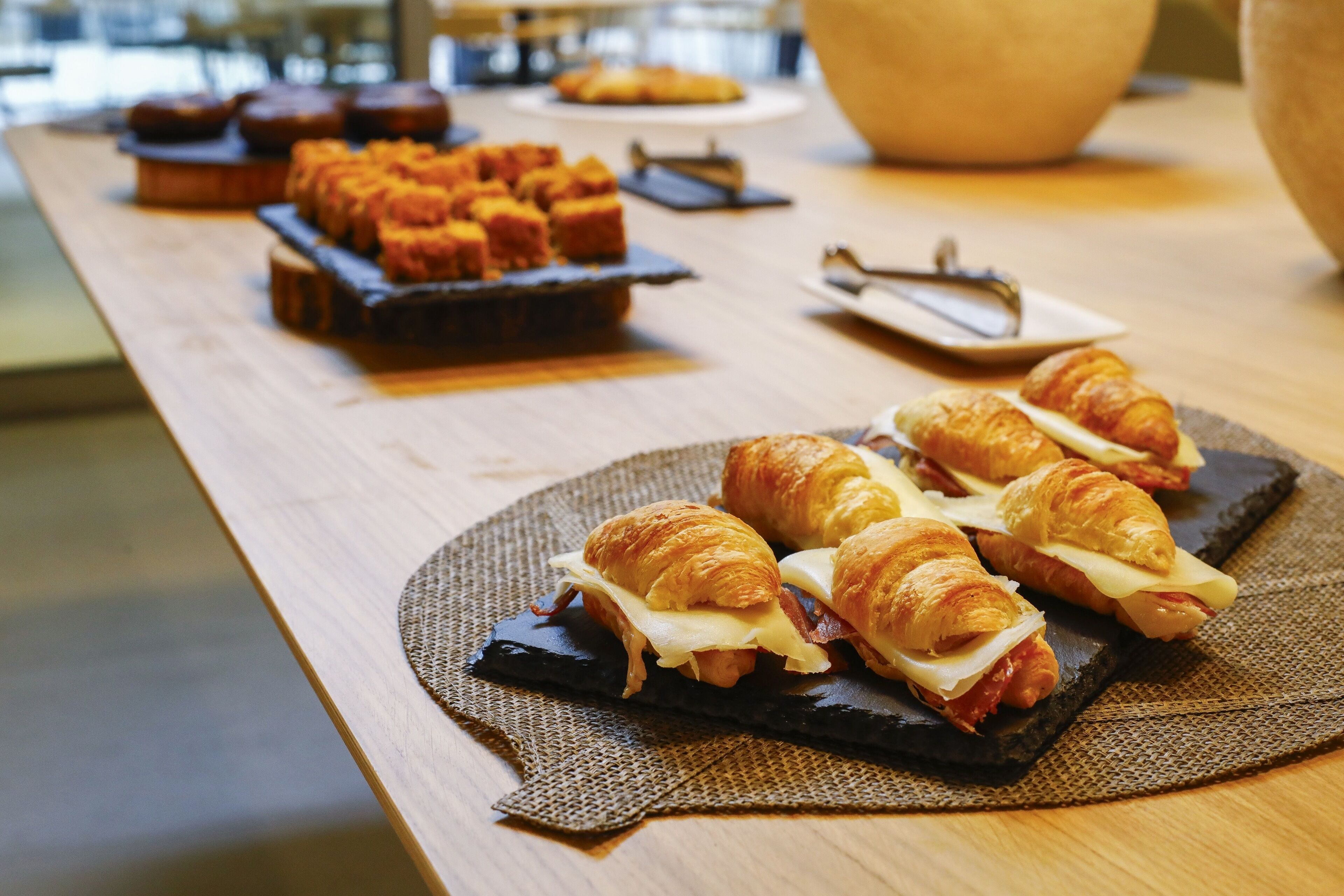 Un bufé de desayuno con cruasanes, sándwiches y muffins sobre una mesa de madera.