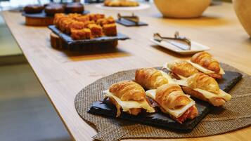 Un bufé de desayuno con cruasanes, sándwiches y muffins sobre una mesa de madera.