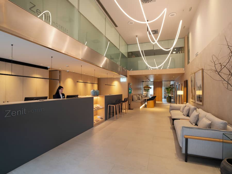 Un moderno vestíbulo de hotel con un mostrador de recepción, zona de estar y una escalera que lleva a los pisos superiores.