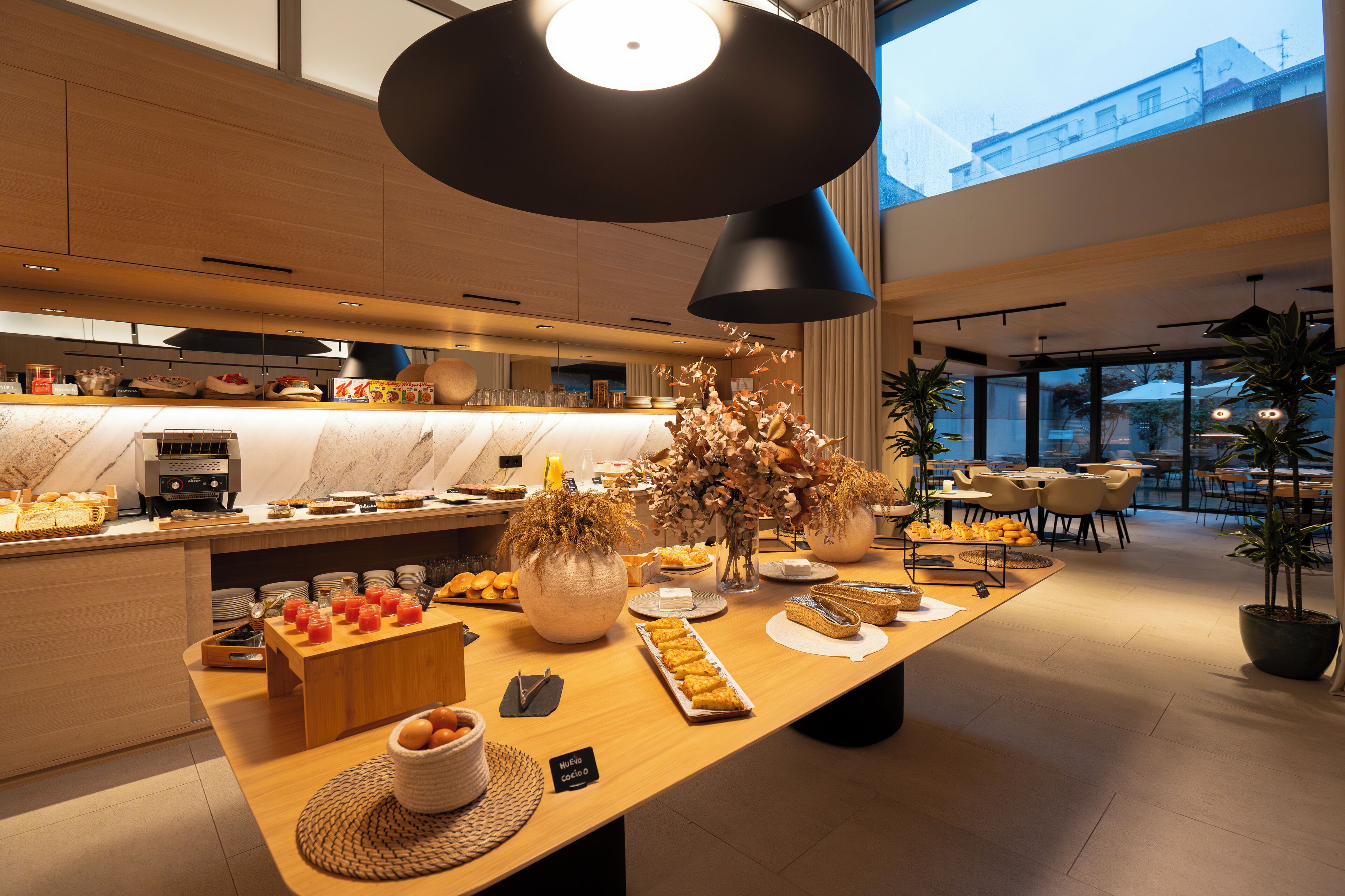 Ein modernes Frühstücksbuffet mit verschiedenen Speisen, einer Kaffeestation und einer Sitzgelegenheit mit Tischen und Stühlen.