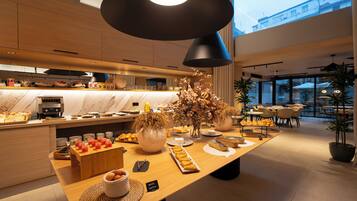 Ein modernes Frühstücksbuffet mit verschiedenen Speisen, einer Kaffeestation und einer Sitzgelegenheit mit Tischen und Stühlen.
