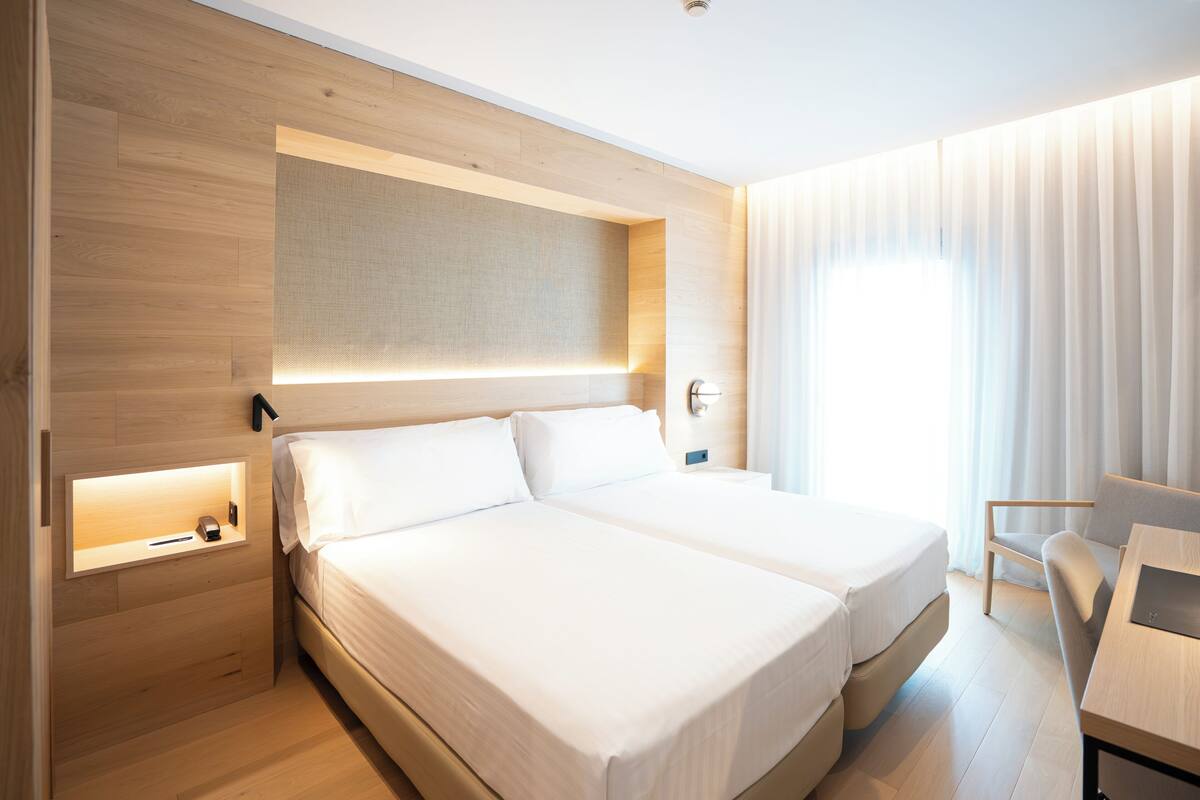 Une chambre d’hôtel moderne avec deux lits, un bureau et une chaise.