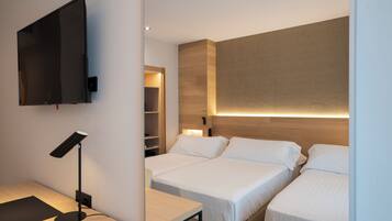 A modern hotel room with two beds, a desk, a TV, and a bedside table with a lamp.