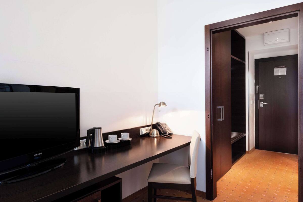 Ein Hotelzimmer mit dunklem Holztisch, Flachbildfernseher, Lampe, Telefon und Stuhl.