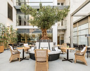 Un espacio interior moderno con mobiliario de mimbre, un árbol grande y una pared de vidrio.
