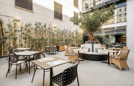 An indoor dining area with bamboo walls, round tables, wicker chairs, and a central seating area with a tree.