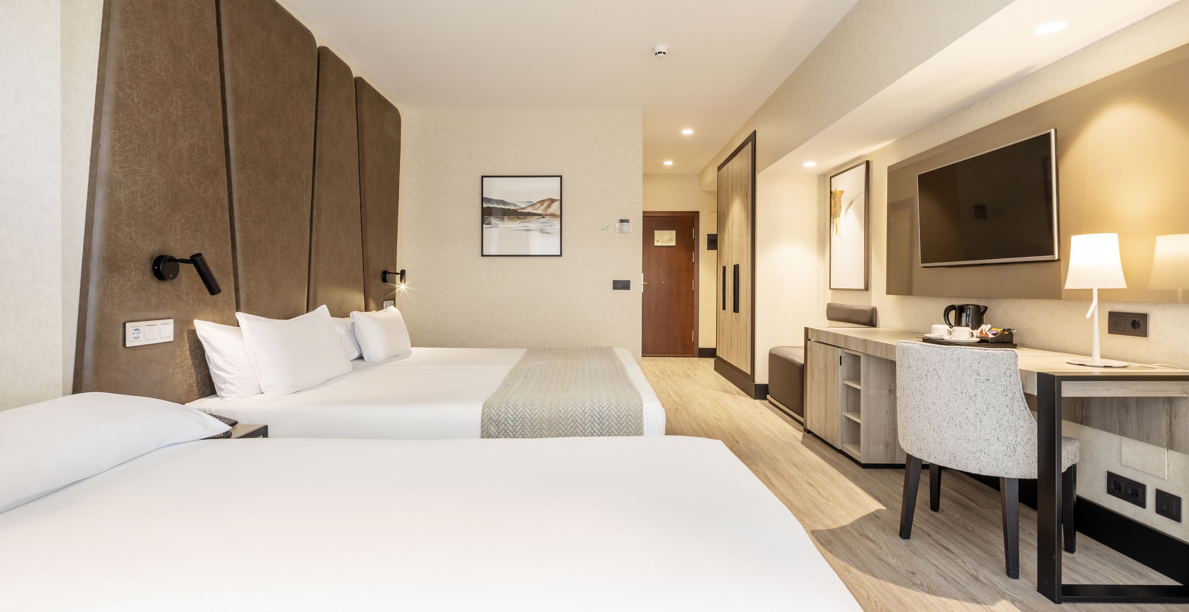 A hotel room with two beds, a desk, a chair, a TV, and a bathroom door.