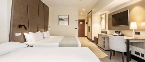 Habitación de hotel con dos camas, un escritorio, una silla, un televisor y la puerta del baño.