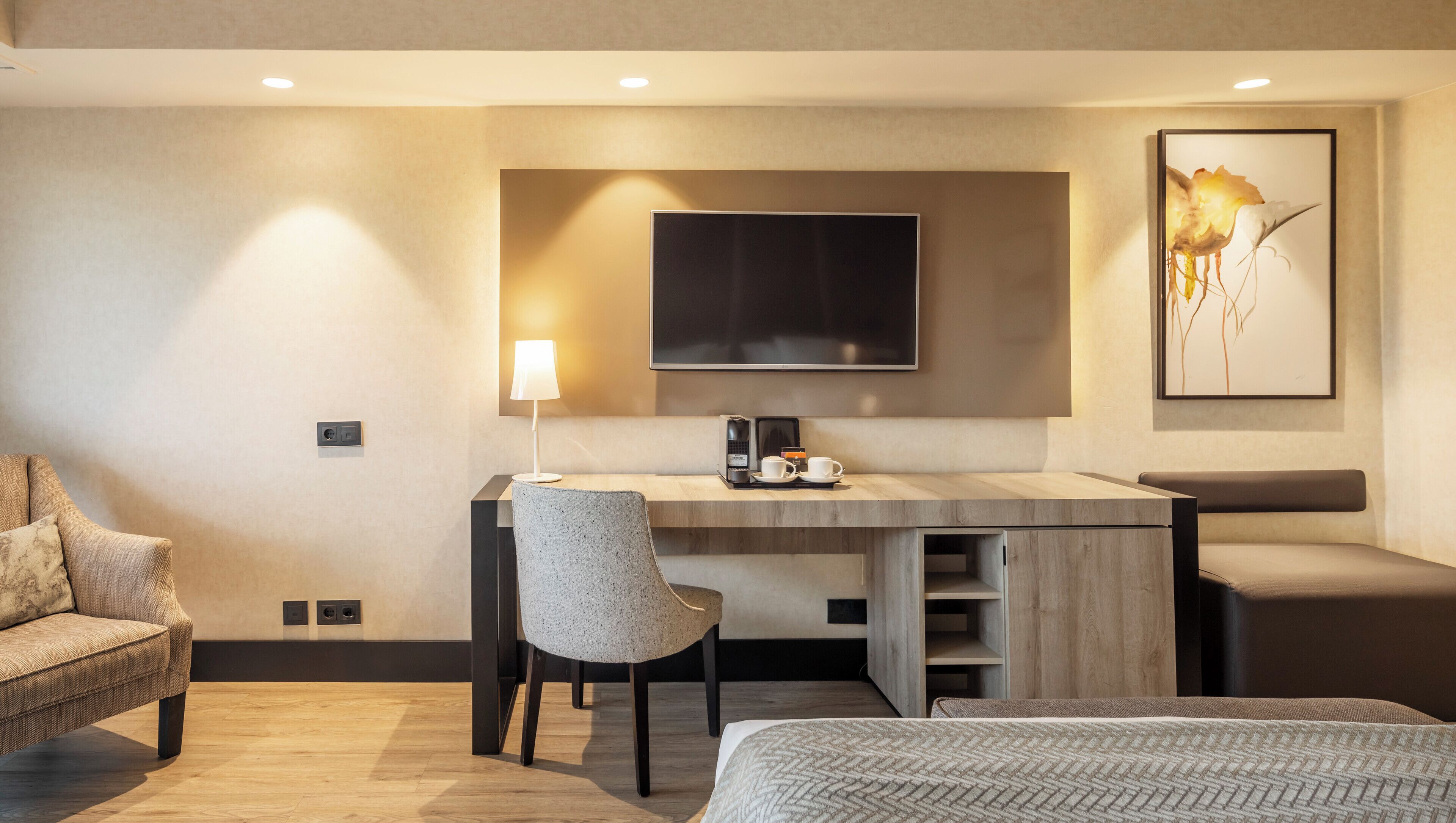 A modern hotel room with a desk, chair, bed, and a large framed artwork on the wall.