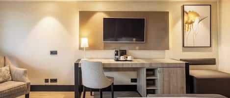A modern hotel room with a desk, chair, bed, and a large framed artwork on the wall.