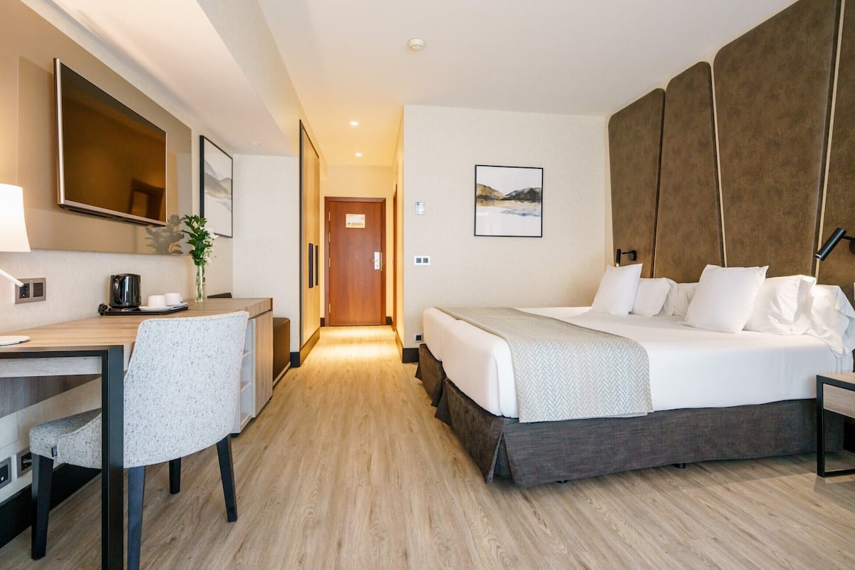 Habitación de hotel con cama, escritorio, silla y un espejo grande.