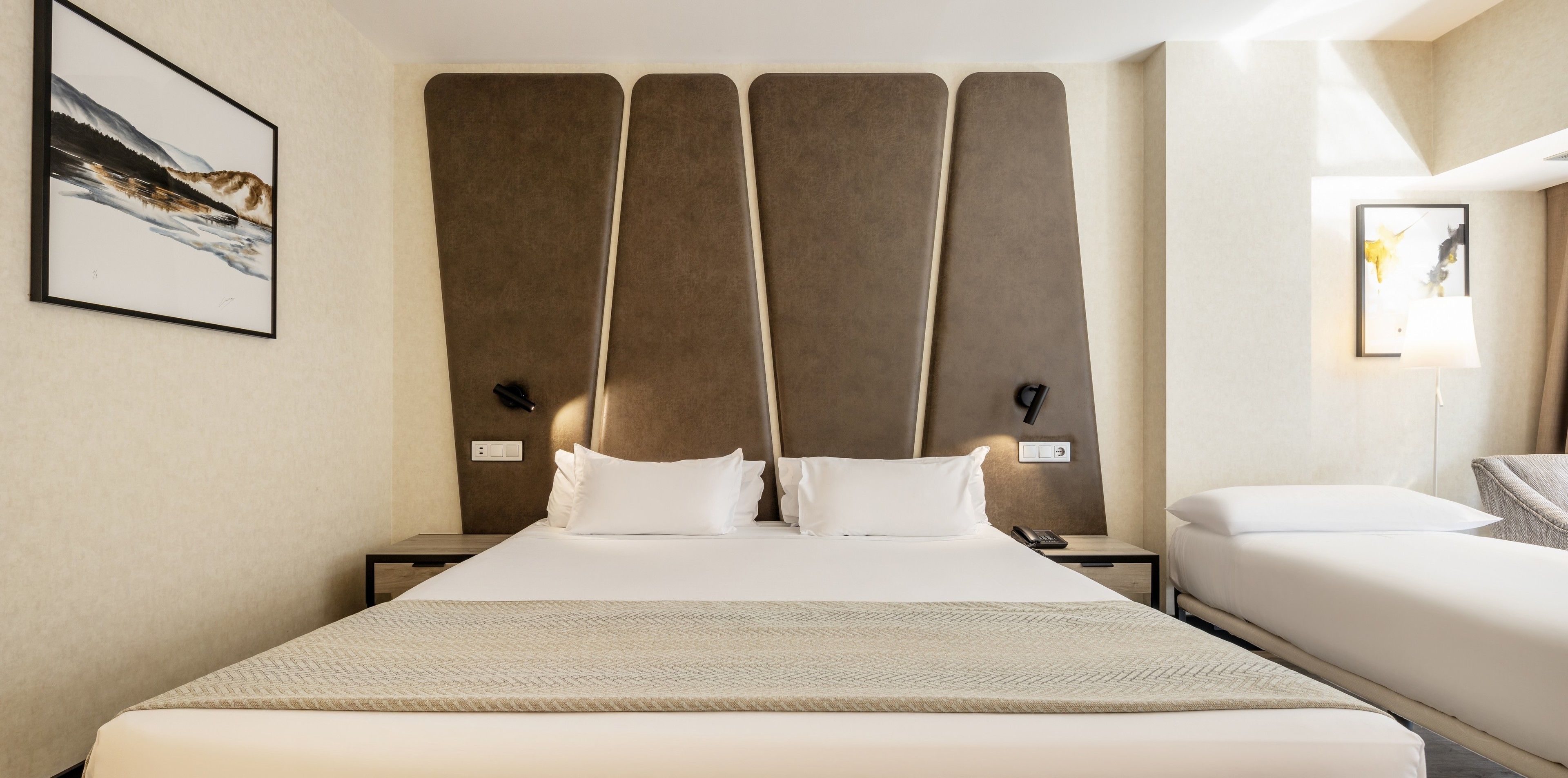 A hotel room with a large bed, two bedside tables, a nightstand, a lamp, and a framed picture on the wall.