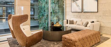 A modern living room with a glass wall, a round coffee table, a sofa, and a tufted ottoman.