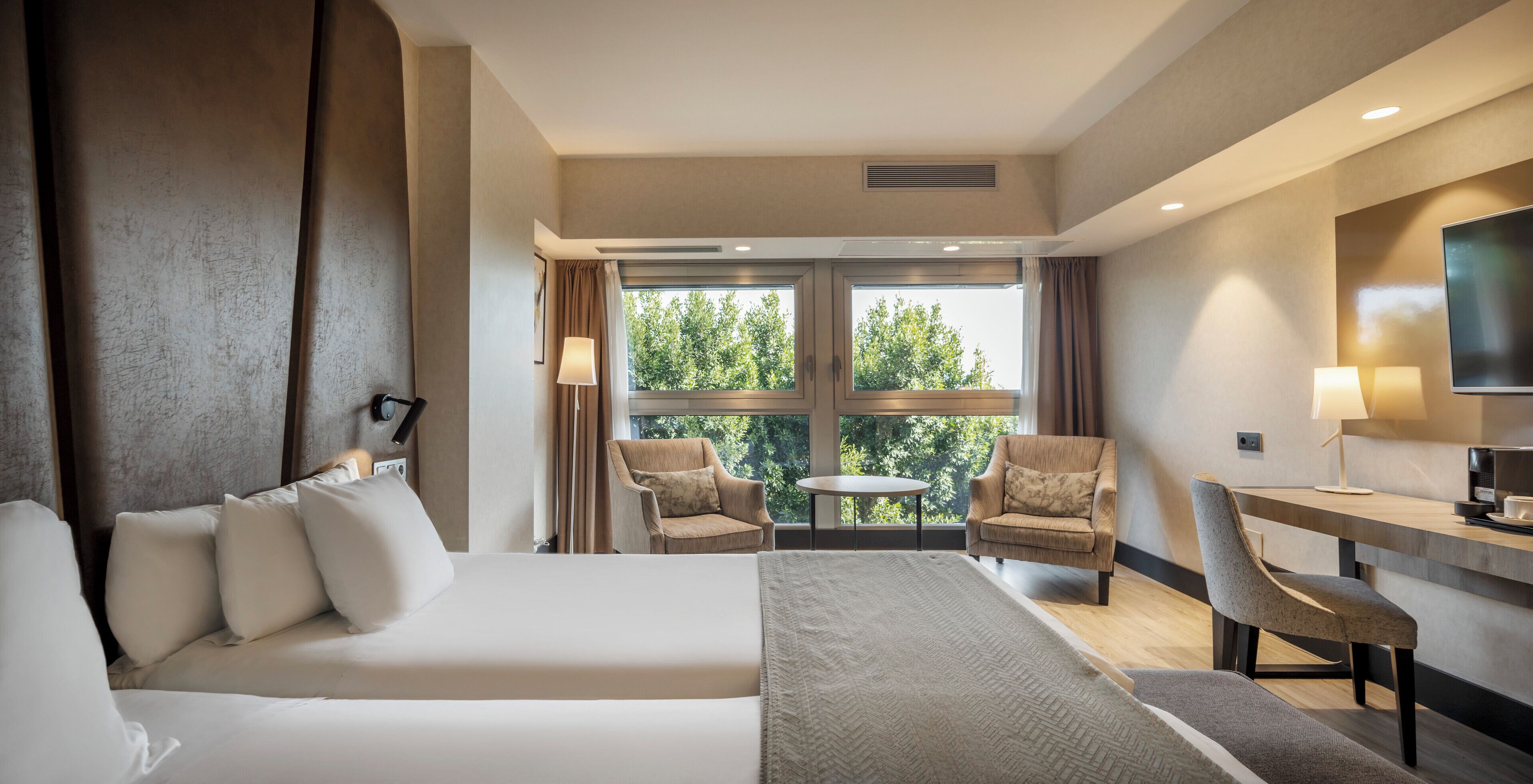 A hotel room with a bed, two armchairs, a desk, and a TV.